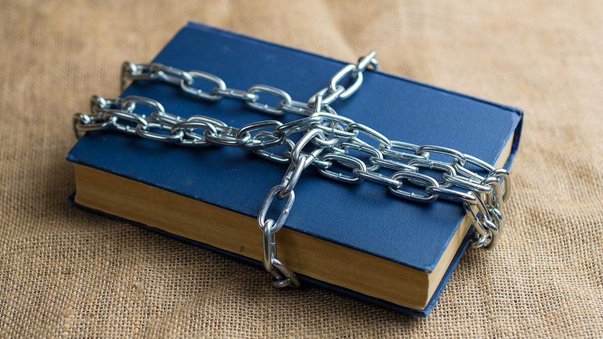 top view of a book in a blue cover lying on burlap, the book is wrapped in a chain, a forbidden banned book read reading censor censorship