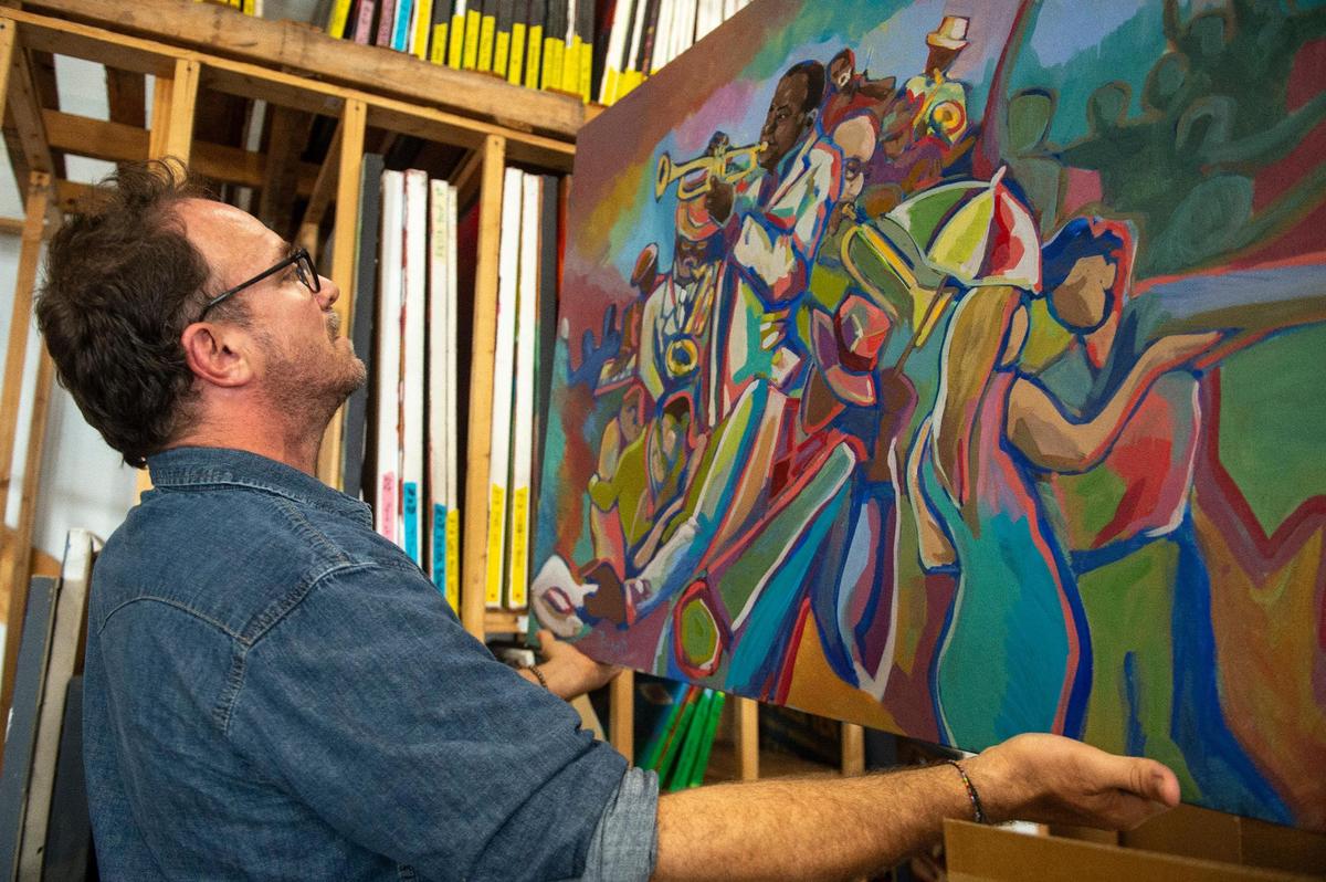 John Bukaty pulls out a completed work of musicians from his collection. Bukaty, who has painted lots of Chiefs-related paintings, also paints live at concerts, including shows of famous musicians.