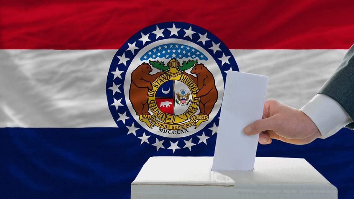 man putting ballot in a box during elections in front of flag american state of missouri