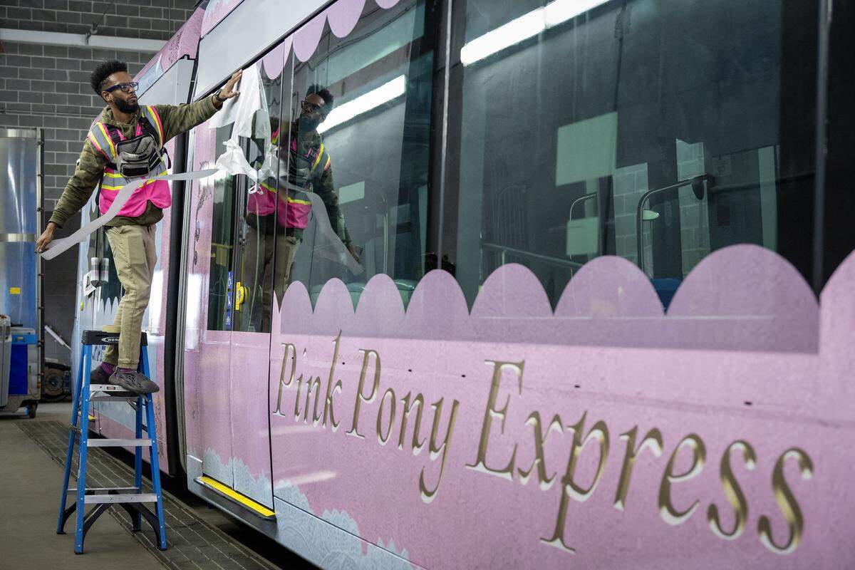 James Holmes IV peels the paper from a vinyl decal to apply it to a to a KC Streetcar being wrapped with a Chappell Roan motif on  Sept. 25, 2025, in Kansas City. The wrap was paid for by the singer to promote her two concerts scheduled for October in Kansas City.