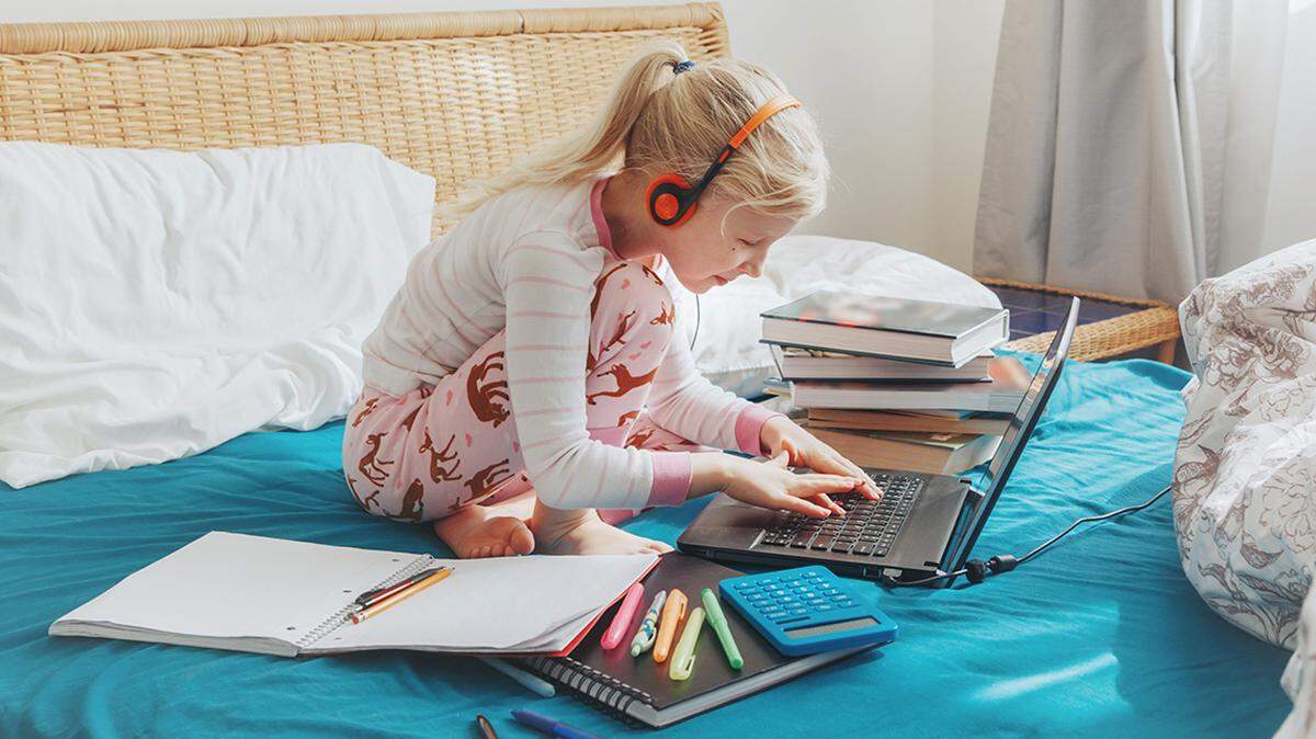 An image of a child working on a computer alone on a bed.