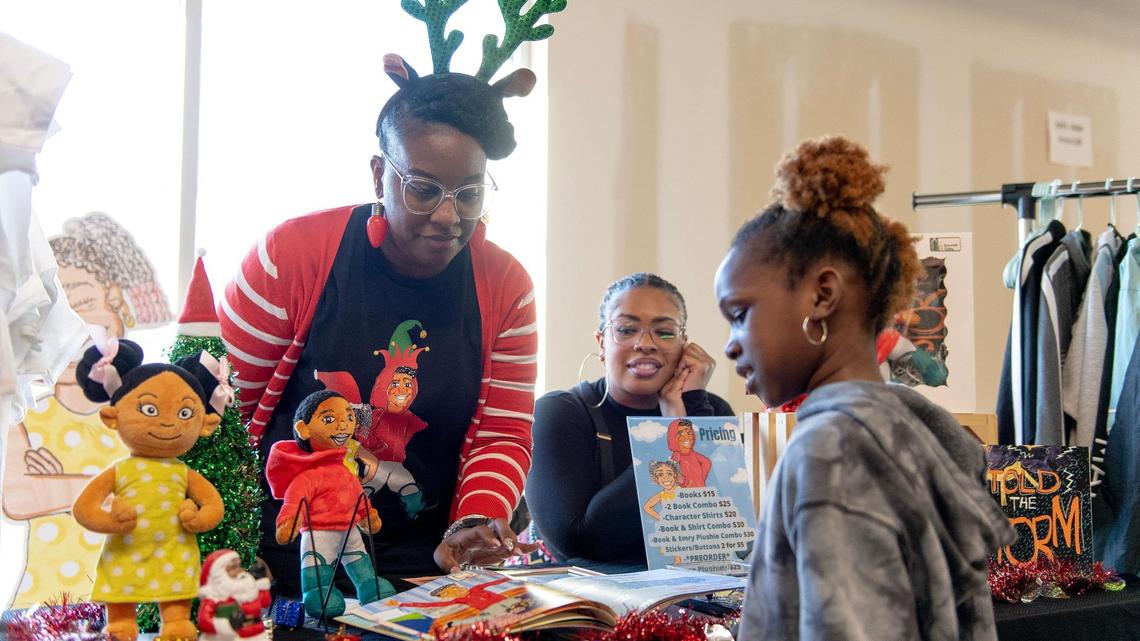 Dayonne Richardson, author of “I Told the Storm” and “Our Gift Grace,” listens as Janiya Woods reads her book at a holiday vendor fair.