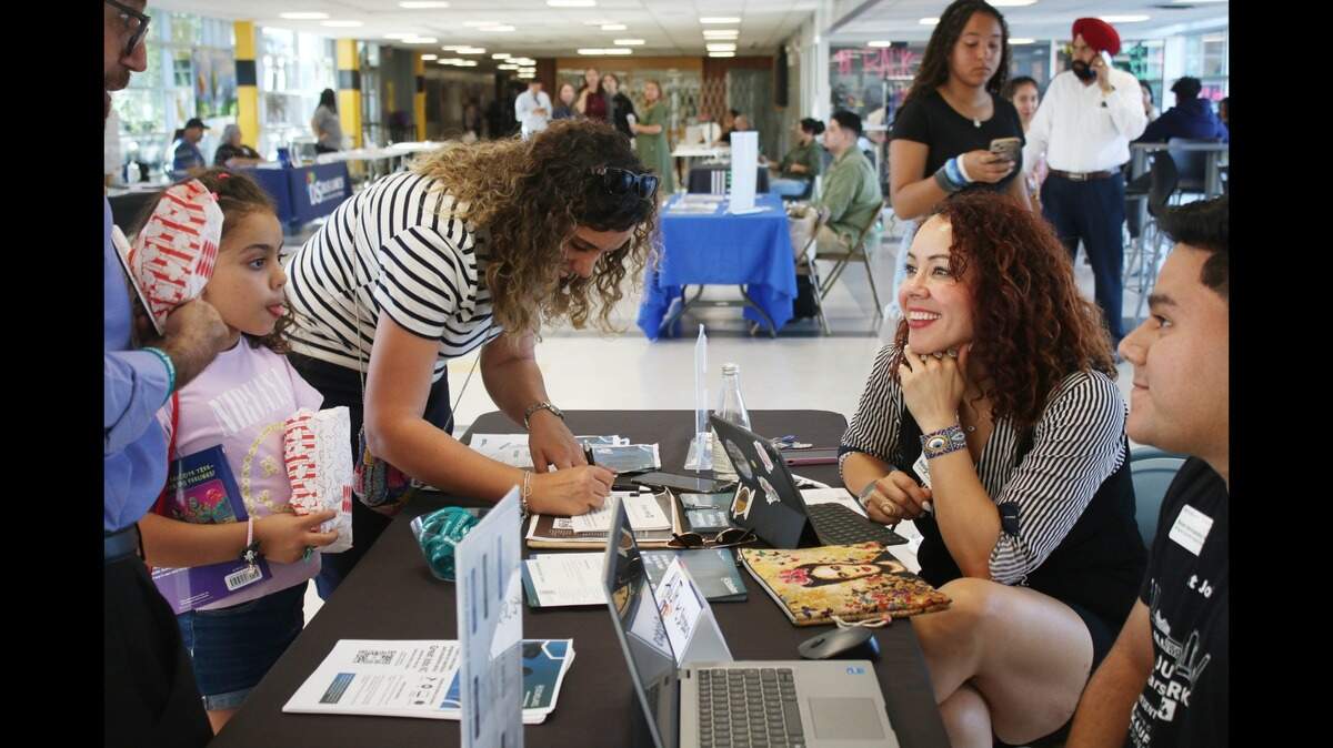 Anais Bouguerra snacks on some popcorn at the Shawnee Mission School District’s multilingual community event as her mom, Hanane Chikhi, gets some information from KC Scholars representatives Rosie Rodriguez and Brian Hernandez.
