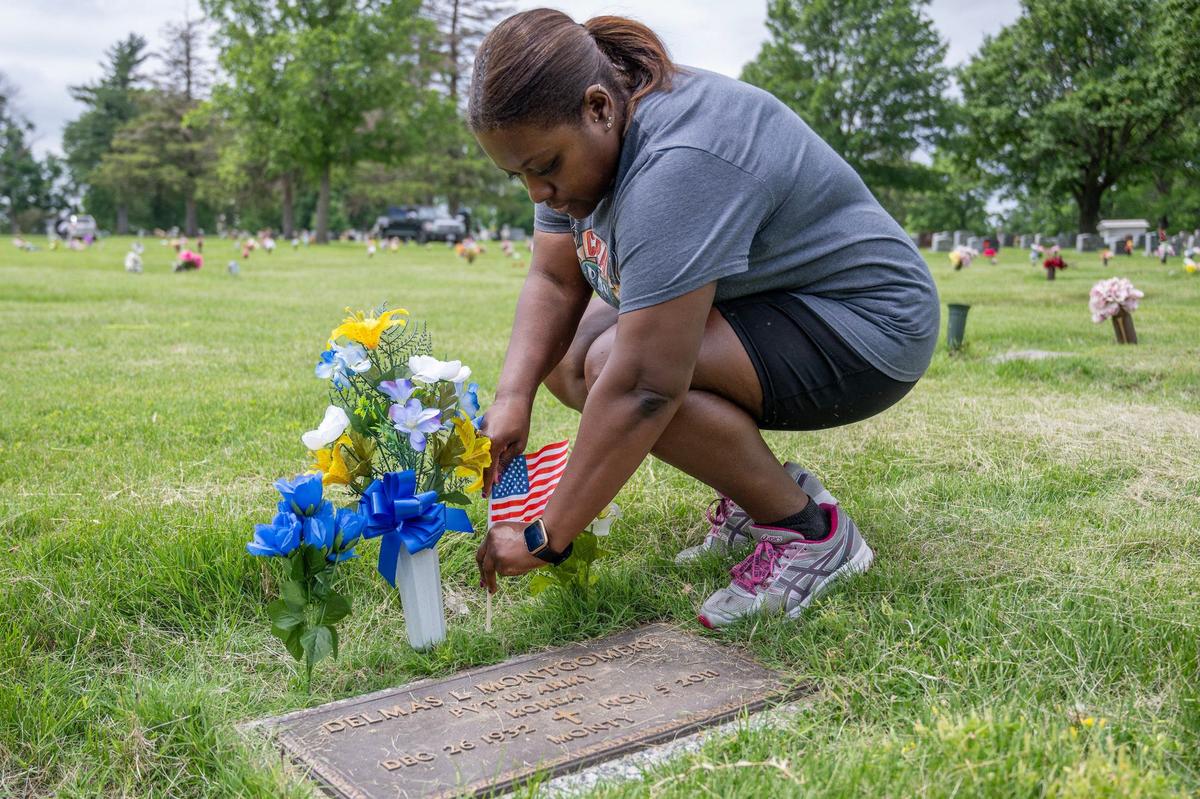 Charla Smith honors her father’s friend, Delmas L. Montgomery, who served in the U.S. Army, by placing a U.S. flag above his grave stone at Forest Hill Calvary Cemetery on Friday, May 24, 2024, in Kansas City.