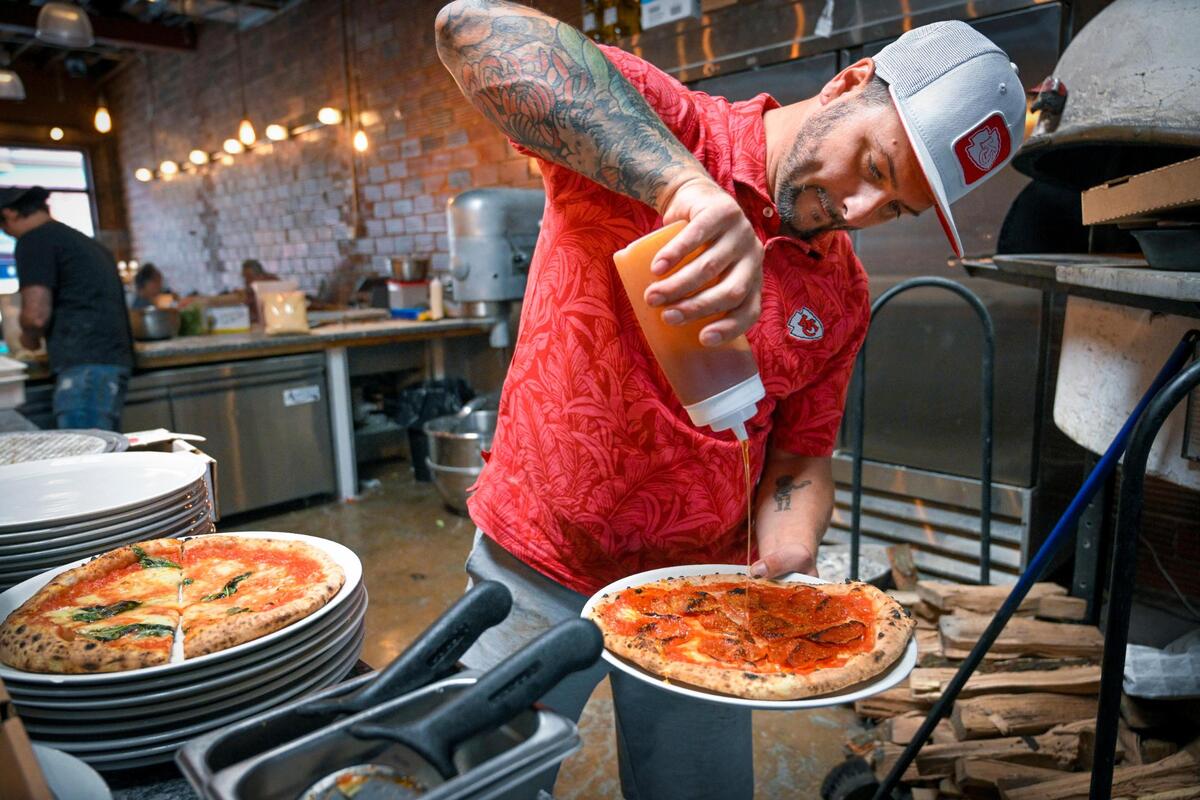 Il Lazzarone owner Josh Young adds a drizzle of spicy honey to a pepperoni pizza, a favorite of Chiefs quarterback Patrick Mahomes. A Margherita pizza sits to the left.