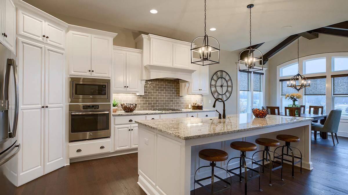 In Riverstone, James Engle Custom Homes garnered First Place for Distinctive Plan and Design on the Fall Parade of Homes with its 1.5-story Sarasota Reverse. This beauty features 4-bedrooms, 4.5-baths, and a large kitchen with sizable walk-in pantry. The spacious Great Room, with floor-to-ceiling see-through stone fireplace, opens to the covered porch.