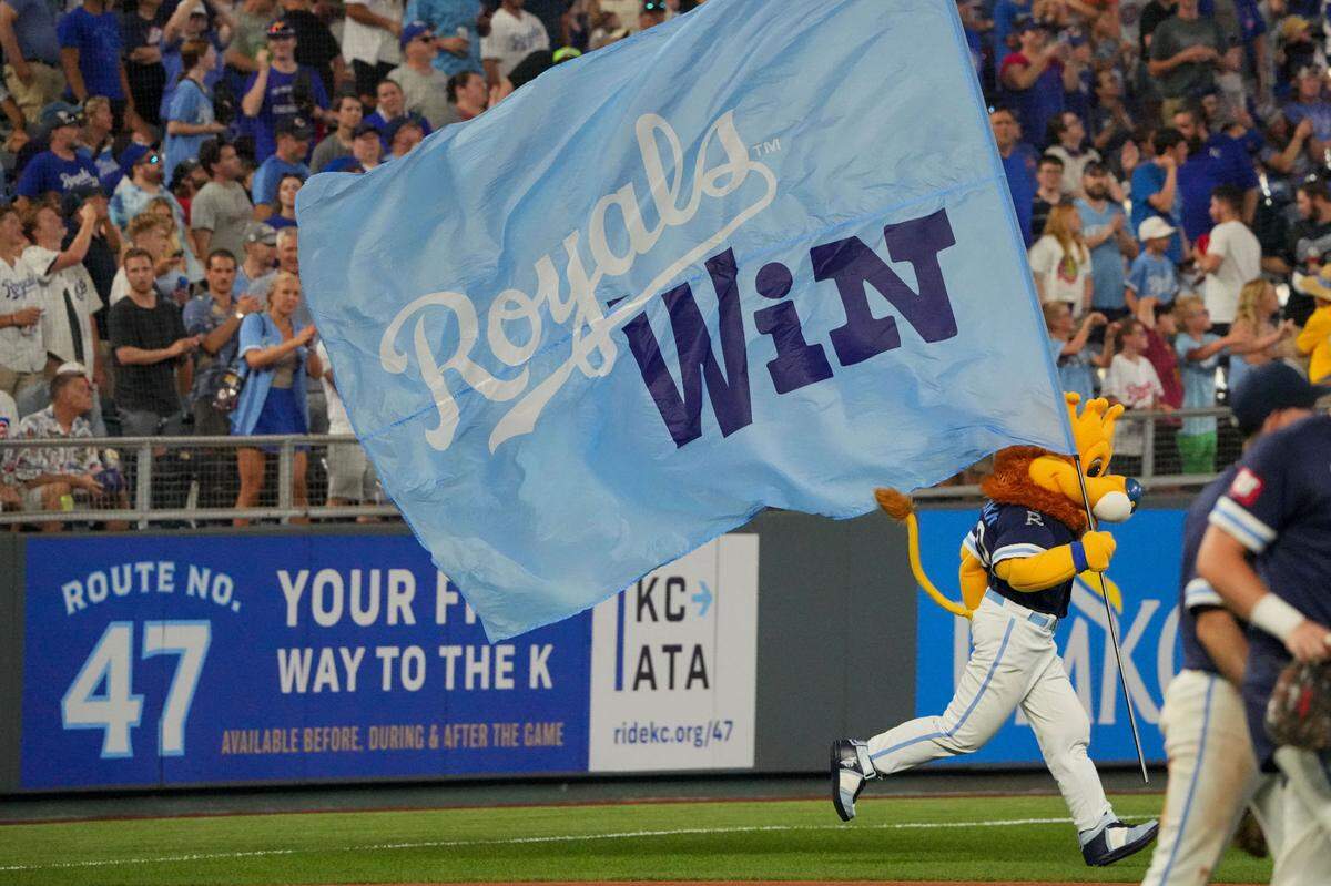 The Kansas City Royals mascot Sluggerrr runs on field with a large sign after the win over the Chicago Cubs at Kauffman Stadium on July 26, 2024.