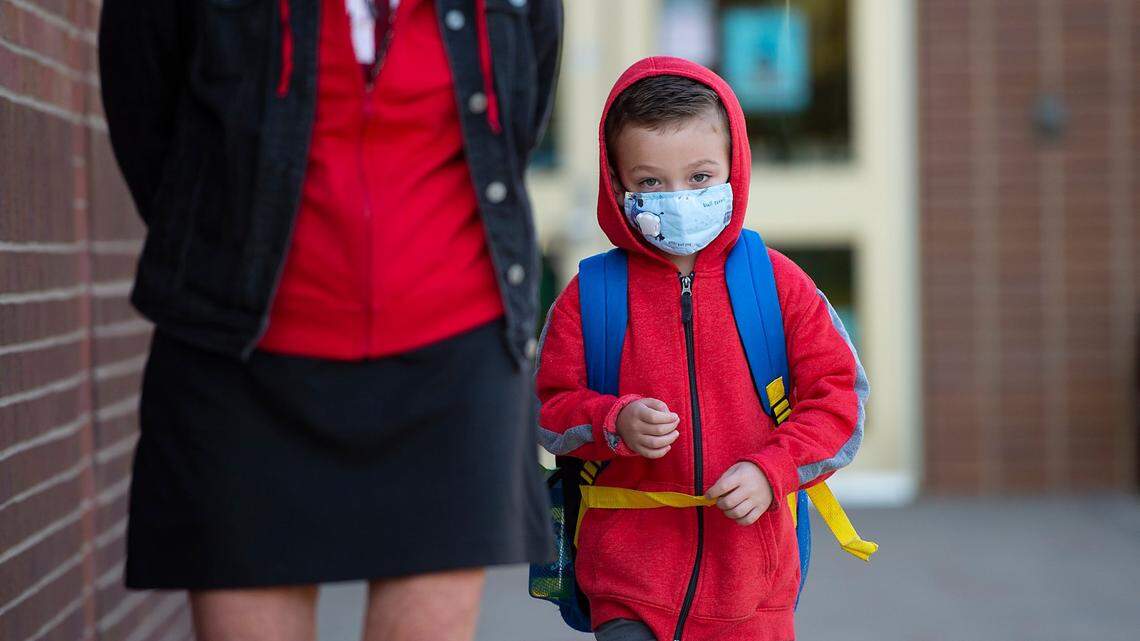 A masked student at Merriam Park Elementary School in Merriam is escorted to his classroom by a teacher on the first day of in-person classes at the school last October.