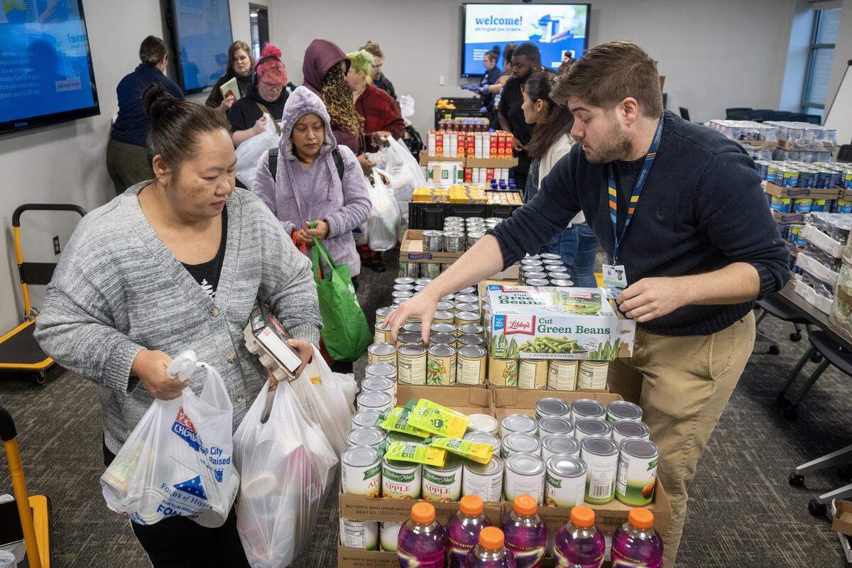 Jan Inth, left, of Kansas City, selected groceries aided by Jacob Glascow, right, during Harvester's monthly food distribution at Jackson County Public Health in Lee's Summit on Wednesday, November 19, 2025. The event aims to help address food insecurity among local residents by providing them with essential groceries.