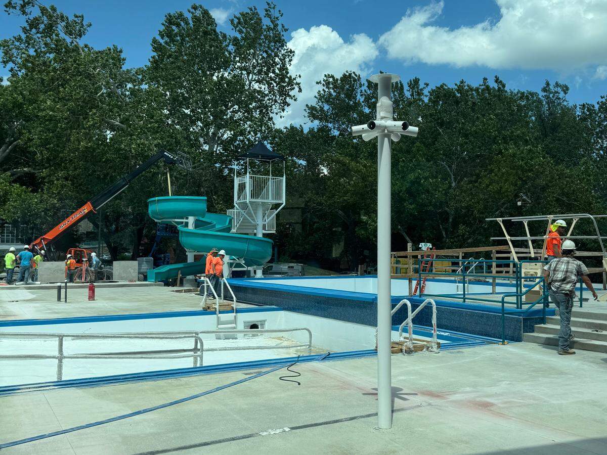 Two unfilled pools and a waterslide are surrounded by construction workers. 