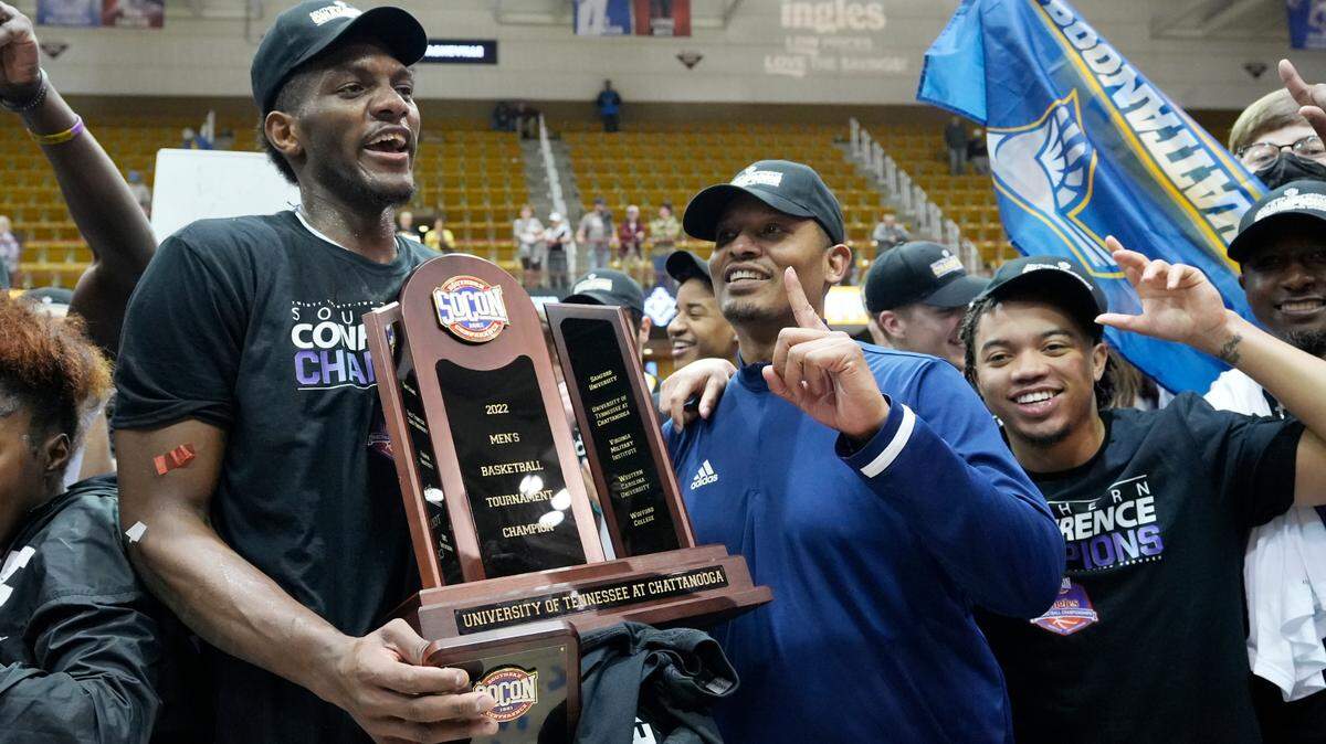 Chattanooga forward Silvio De Sousa, left, and head coach Lamont Paris hold the championship trophy to celebrate their win over Furman in an NCAA college basketball championship game for the Southern Conference tournament, Monday, March 7, 2022, in Asheville, N.C. (AP Photo/Kathy Kmonicek