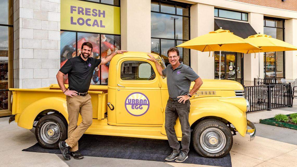 Urban Egg owners Brennan Price, left, and his dad, Randy Price, stood with the chain’s 1942 bright yellow Chevy truck Monday outside the new location of their restaurant in Hawthorne Plaza, 4921 W. 119th St., in Overland Park.