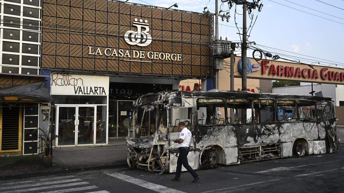 A police officer walks next to a burned-out bus in Puerto Vallarta, Jalisco state, Mexico, on February 23, 2026. Mexico has deployed 10,000 troops to quell clashes sparked by the killing of the country's most wanted drug lord, which have left dozens dead, officials said on February 23.