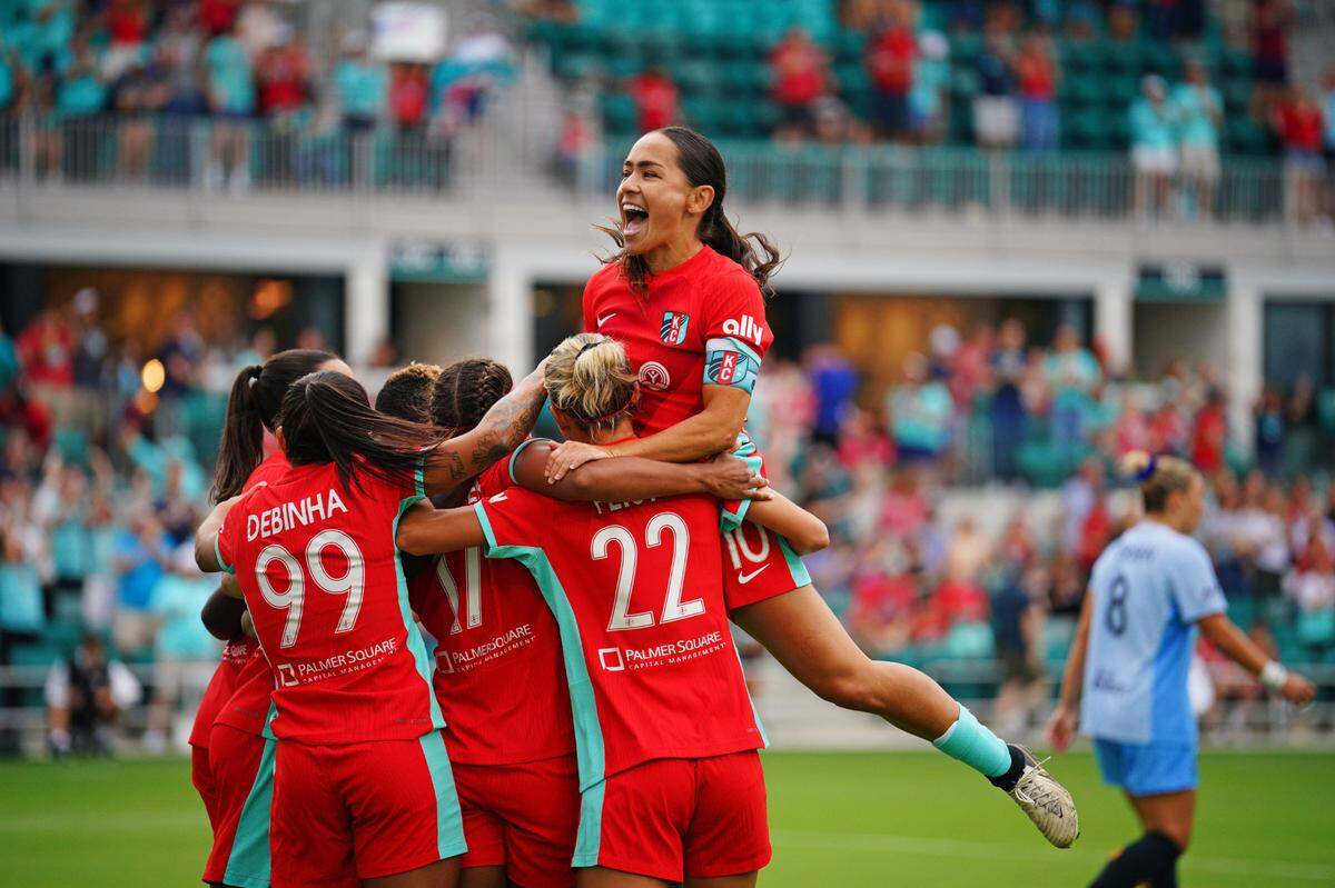 Kansas City Current forward Michelle Cooper (17) is mobbed by teammates after scoring a goal during the first half against the Houston Dash at CPKC Stadium on July 20, 2024.