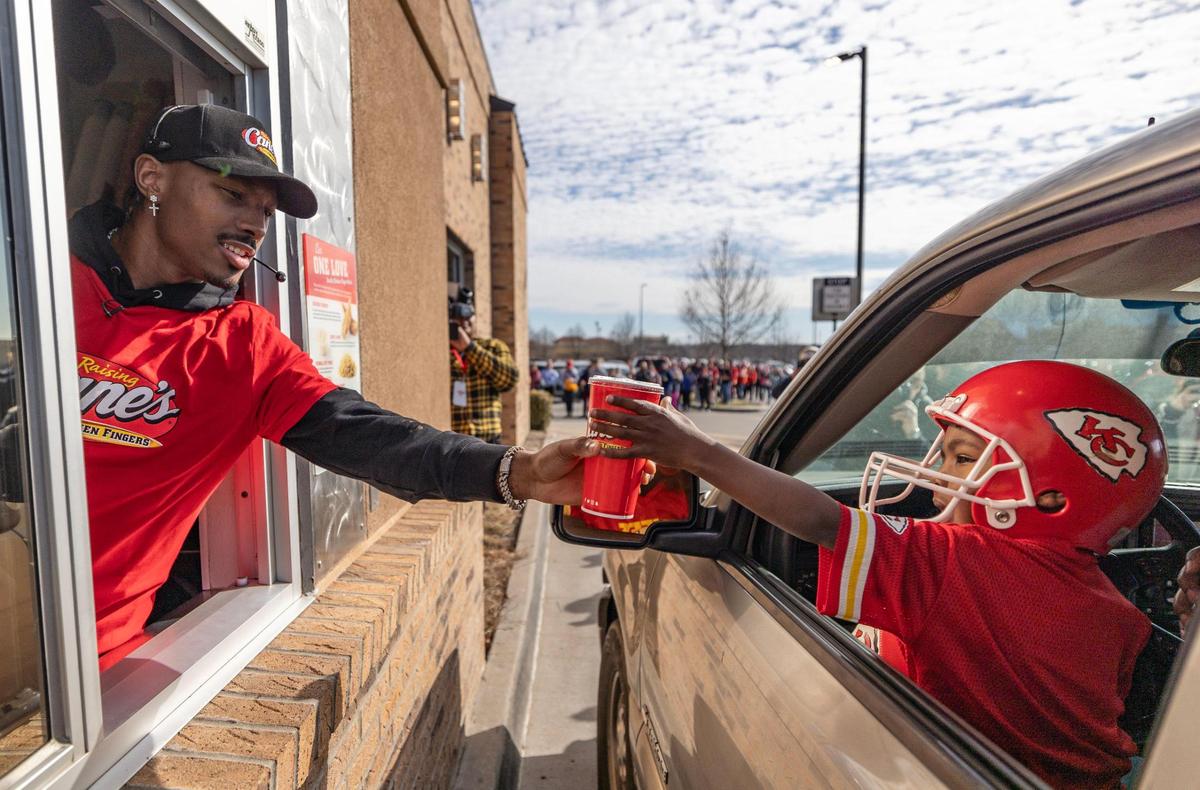 Kansas City Chiefs receiver Mecole Hardman Jr. hands a drink to a young Chiefs fan while working the drive-thru at a Raising Cane’s restaurant in Blue Springs on Tuesday. Hardman was joined by teammate L’Jarius Sneed at the event.