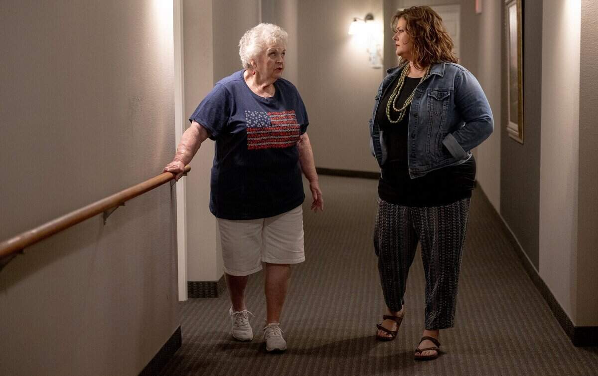 Jeannine Binder, left, and end-of-life doula Ashley Boydston stroll the hallways of Binder’s condo building. Binder’s family asked Boydston to continue to visit her after her husband died in April.