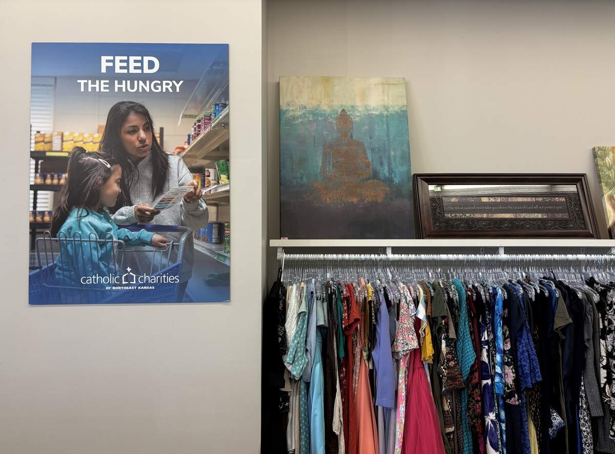 Wall art sits on a shelf above a rack of dresses. A sign on the left reads “Feed the hungry.”