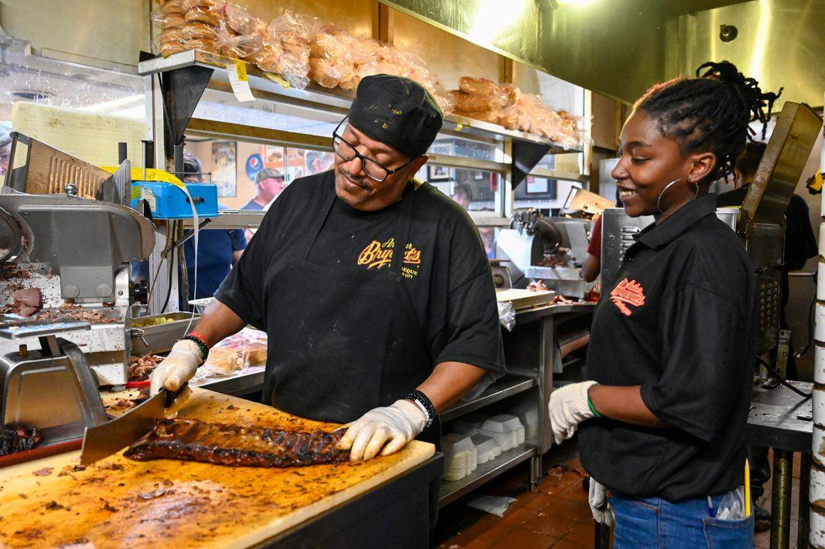 Larry Ashley wields a large knife as he slices a slab of ribs while manager Raven Watts looks on in the kitchen at Arthur Bryant’s Barbeque.