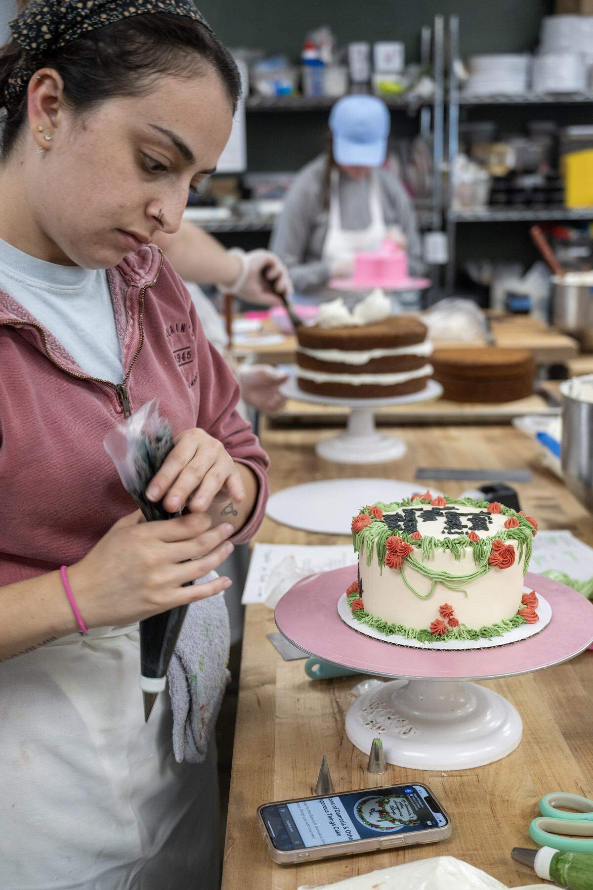 Cake decorator Hannah Finch glances at the design for a "Visions of Damsels & Other Dangerous Things,” a Chappell Roan-themed cake she was making at McLain's Bakery in Waldo on Thursday, October, 2, 2025.  Local bakeries are seeing a significant demand for cookies to celebrate pop stars Taylor Swift and Chappell Roan. 