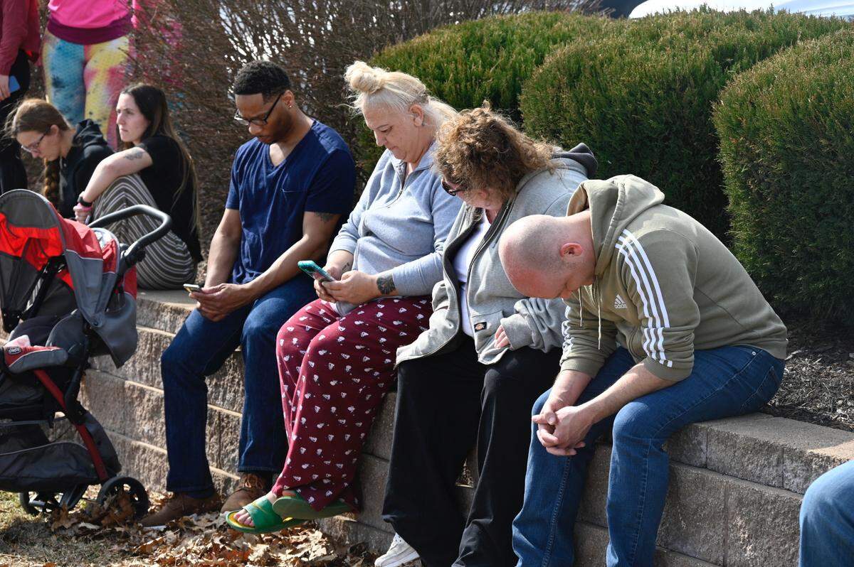 Neil Moore, head down, waits with other Olathe East High School parents for their kids at a reunification site at 127th and South Blackbob Friday after a shooting at the school. He was talking to his freshman son on the phone when it happened, he says his son didn’t hear anything about a shooting but heard an announcement that the school was on lockdown.