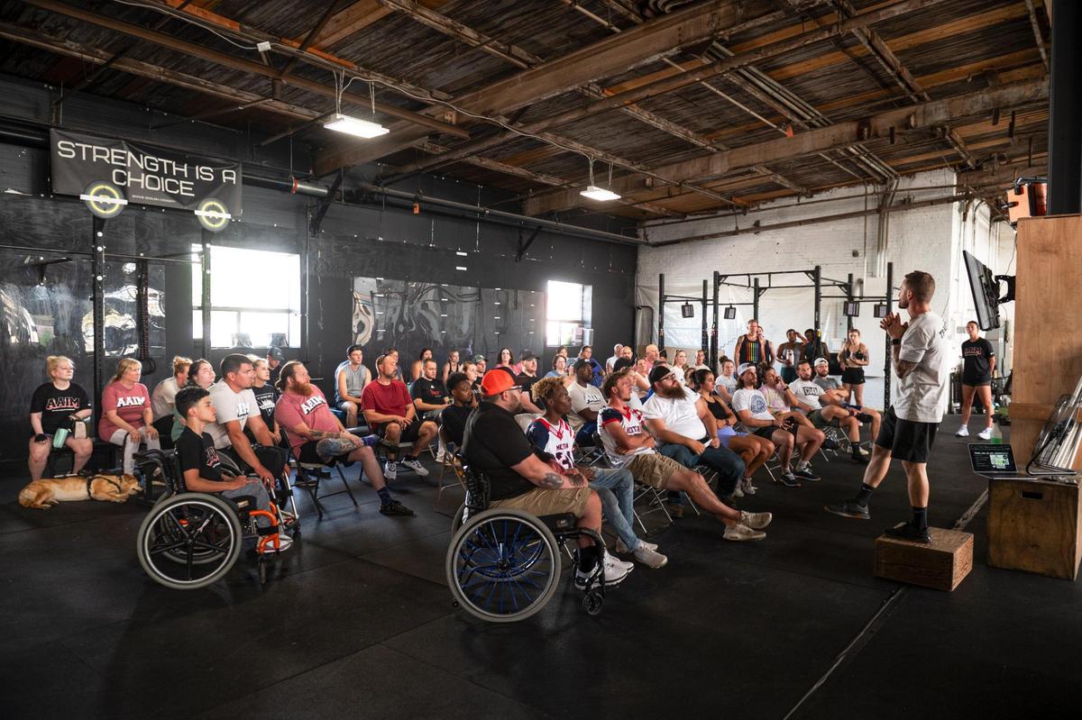 Attendees of an Adaptive Athletes in Motion fundraising event listen to founder Josh Snyder, right, speak at Brave Enough CrossFit in Kansas City. The event was hosted so athletes without disabilities could experience the training regime for the athletes with disabilites.