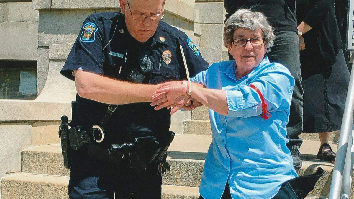 Sister Barbara McCracken of the Benedictine Sisters of Mount St. Scholastica in Atchison, Kansas, being arrested in 2018 and led from the office of then-Secretary of State Kris Kobach.