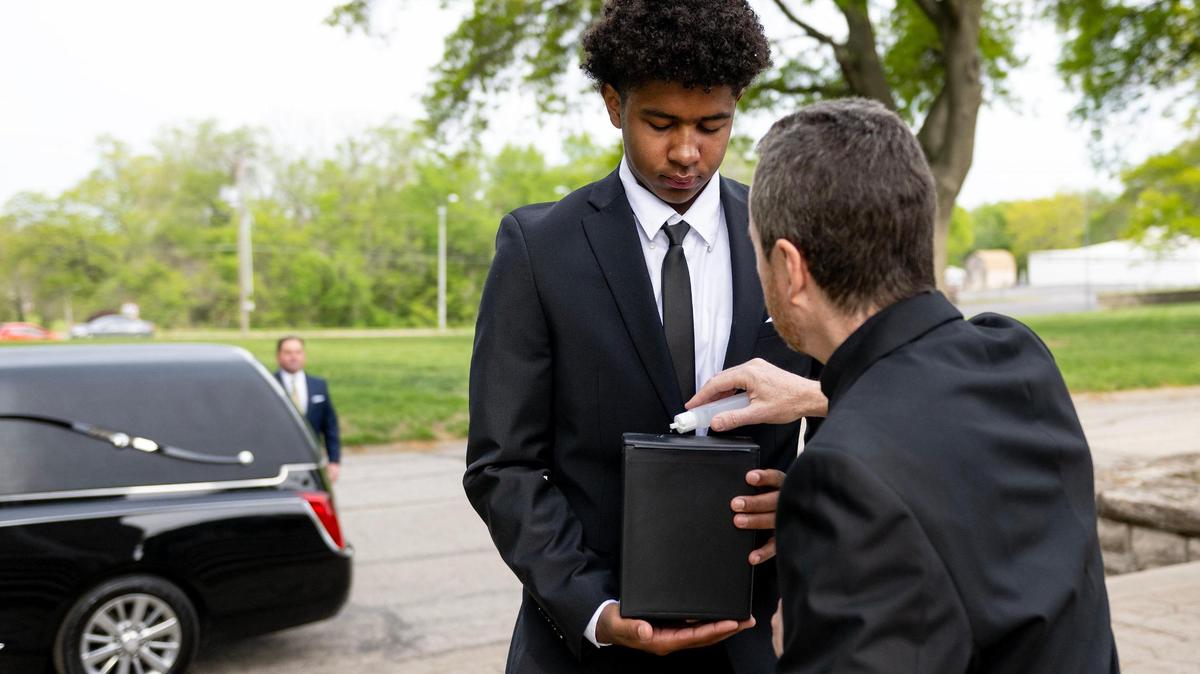 The Rev. Gary Menard blesses a cremated body with holy water as Myles Carson carries it to its final resting place during a funeral service for unclaimed deceased persons at the Mount Olivet Catholic Cemetery in Raytown.