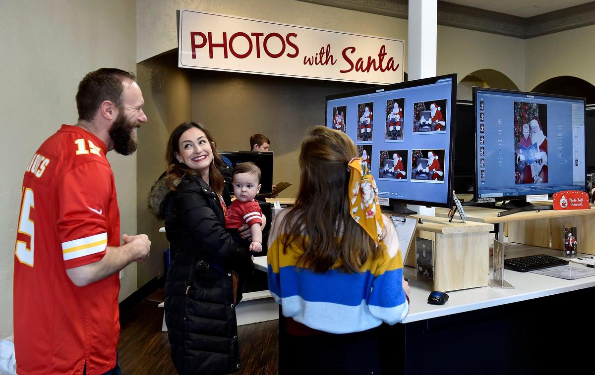Andrew and Brecklyn Wright of Overland Park, left, with their son Harlan, select photos with sales associate Samantha Kopecky at Jordan Photography in Leawood. Owner John Jordan has had to hire more Santas to meet the increased demand. Customers can even select their Santa, all of whom have real beards.