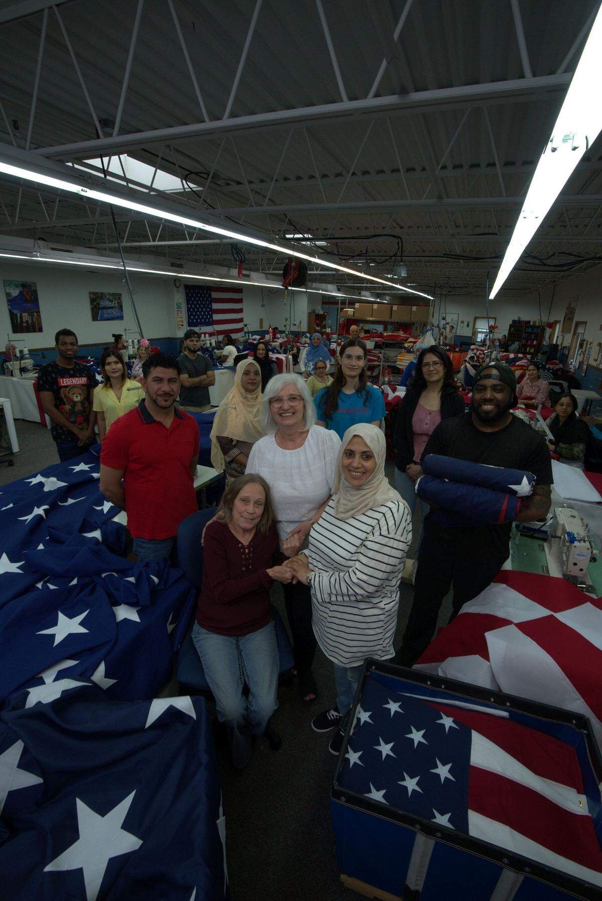 Smiling on the Eder Flag factory floor, from left: Hazarah, Amanda, Thay Le, Rajka, Ali, Hector, Jakitha, Wajeda, Sughra, Barbara, Carlixta, Radica, Shahnaz, Maria, Evelia, Aijaz, Jean, Lamyaa, Omaima, Lida, Mahida, Nant, SugarRay, Vimmi and Raheela.