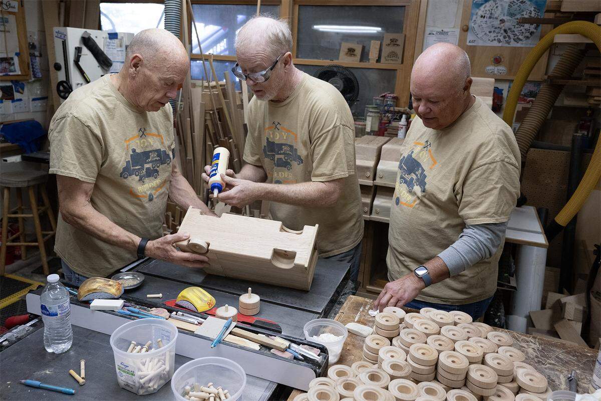 Jay Morris of JHM Woodworks, center, works with volunteers Steve “Woody' Wood, left, and Tony Kisner, as they transform donated wood scraps into toy trucks on Tuesday, Dec. 2, 2025 in Lawrence, Kansas. Morris will donate 115 handmade trucks that will reach kids in need through Toys for Tots program.
