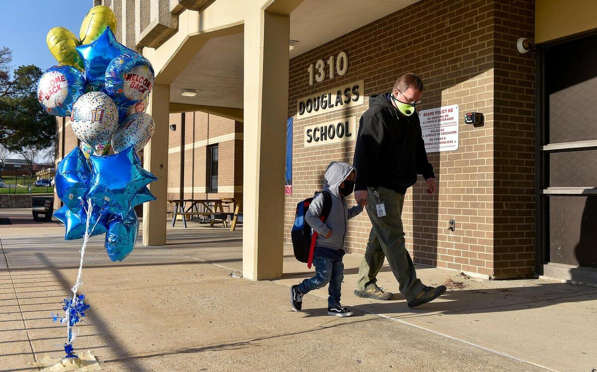 Joe Page, technology teacher at Douglass Elementary School in Kansas City, Kansas, walks a kindergartner who Page said had never taken the bus before, into the building. Students arrived for the first day of full in-person learning Wednesday, March 31, 2021. According to Principal Louis Neal, about 75 percent of students are coming back for in-person learning.