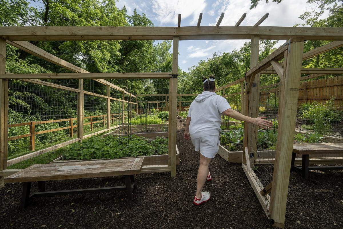 Cariann Lile, 56, walks into the community garden at Eden Village of Kansas City on Tuesday, May 12, 2026, in Kansas City, Kansas. Lile, who experienced homelessness for six years before moving into the community in September 2024, says the stability home and her new community,  feels like "winning the lottery."