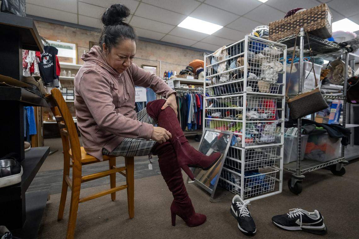 Betzaida Sanchez of Kansas City, Kansas, tries on a pair of thigh-high burgundy suede boots during a visit to Troost39 Thrift Store, 3922 Troost Ave., on Thursday, Jan. 15 2026, in Kansas City. Sanchez said she planned to purchase the like-new boots for $8.00. 