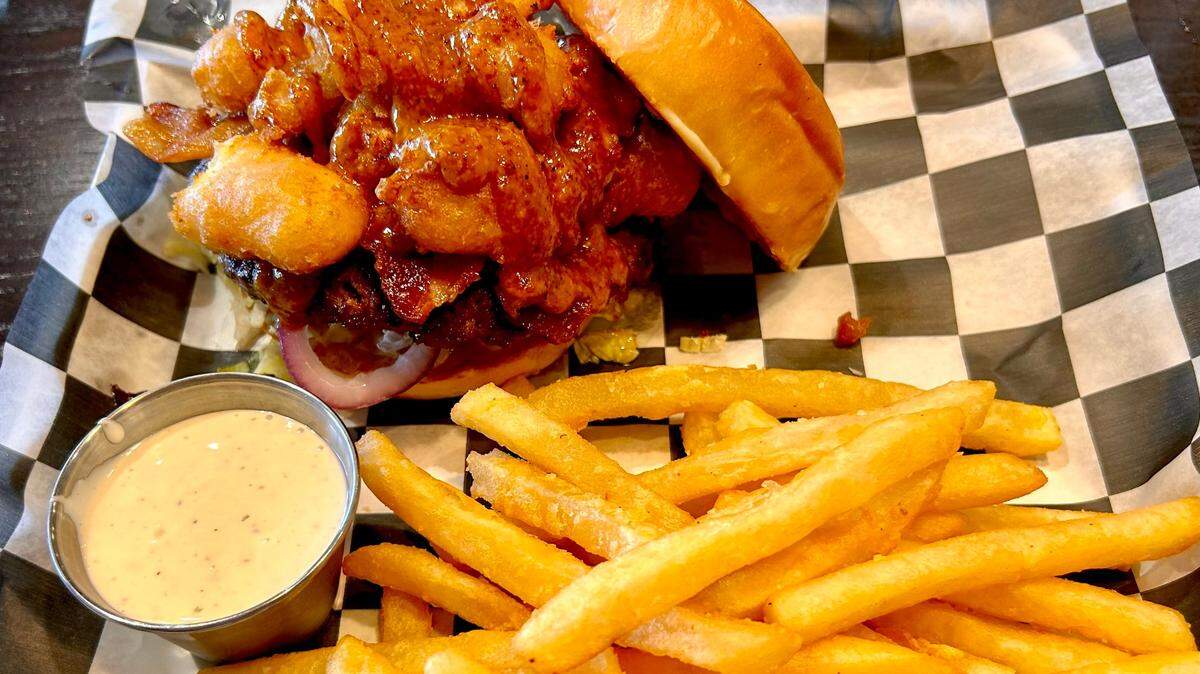 The Crush Burger is topped with bacon, cheese curds, chipotle honey mustard, garlic aioli, lettuce, red onions and tomatoes.
