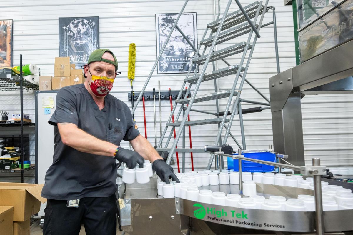 Richard Peterson loads empty containers onto a conveyor belt that will fill the containers with marijuana at the farm and production facility of Illicit Farms.