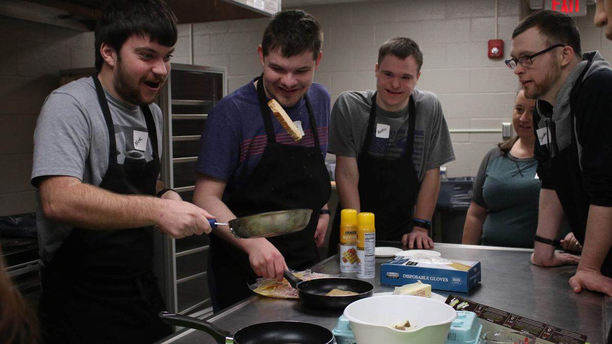 Nick Pettigrew flips a piece of toast in a frying pan as Kyle West, Austin Tomandl, Riki Kisner and Jacob Tomandl watch during an adaptive cooking class at the Shawnee Civic Center.