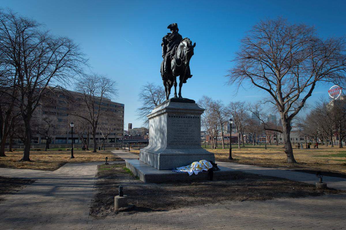 The George Washington Memorial shades a houseless person sleeping at its base. March 29, 2023.