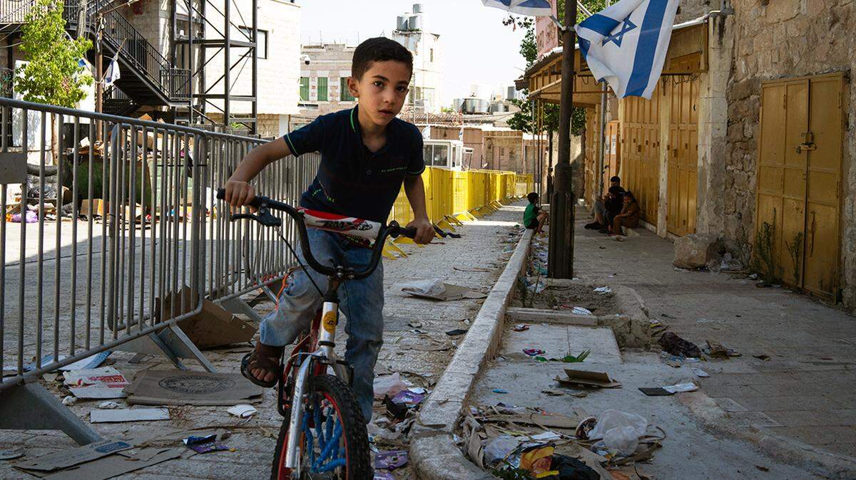 A Palestinian boy rides his bike alongside Israeli flags and barriers blocking access to Jewish-only colonies, near Al Ibrahimi Mosque/Cave of the Patriarchs in Hebron, Palestine.