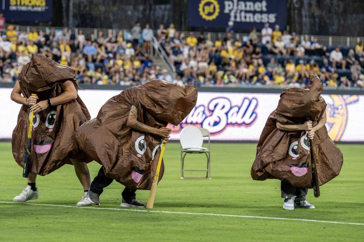 Fans dressed as poop emojis spin on a bat during a Banana Ball in-game entertainment segment between the Savannah Bananas and the Indianapolis Clowns at Kauffman Stadium Saturday, May 30, 2026, in Kansas City.
