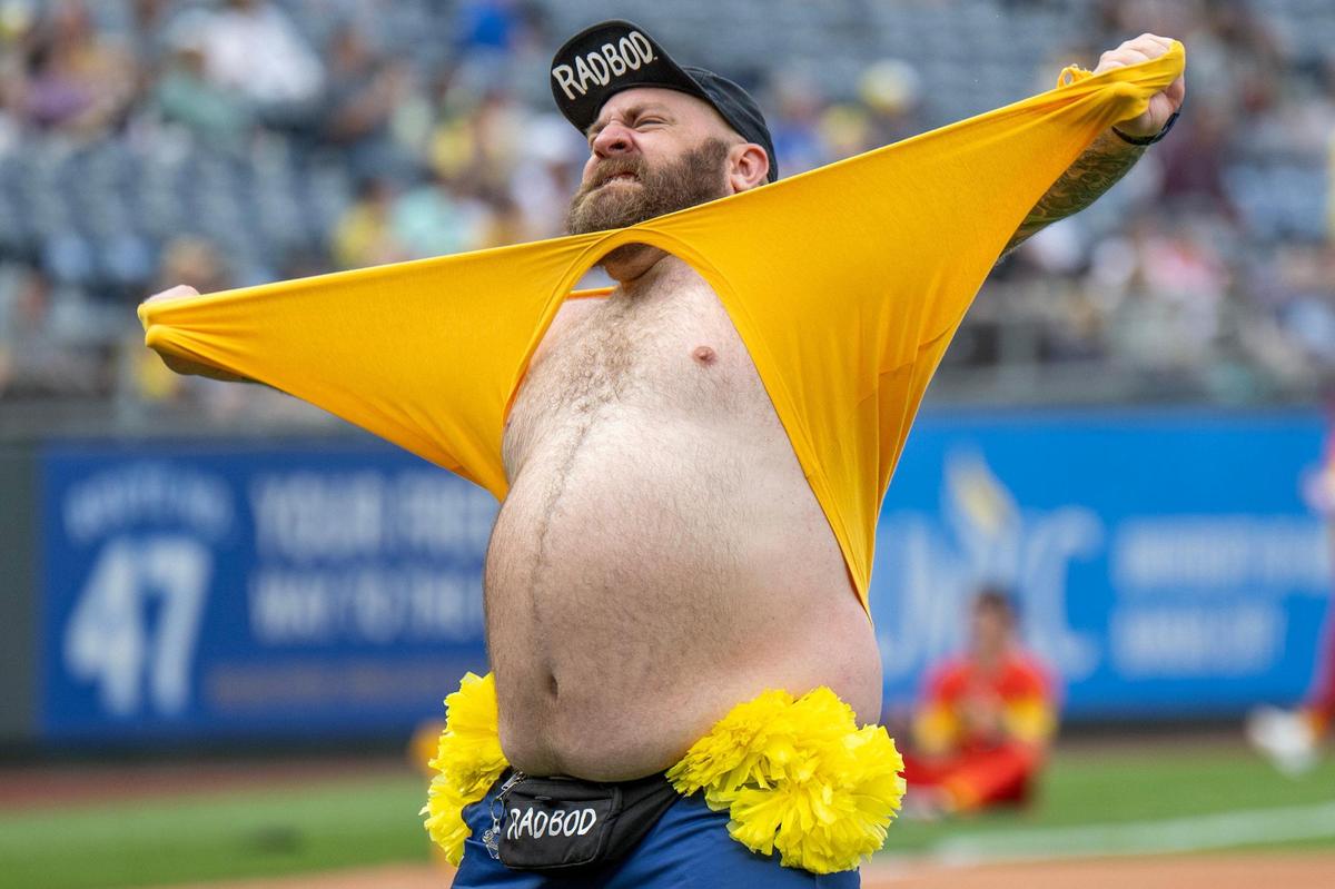 A member of the Savannah Bananas’ Dad Bod Cheer Squad rips their shirt before a Banana Ball game against the Firefighters at Kauffman Stadium on Friday, May 23, 2025, in Kansas City.