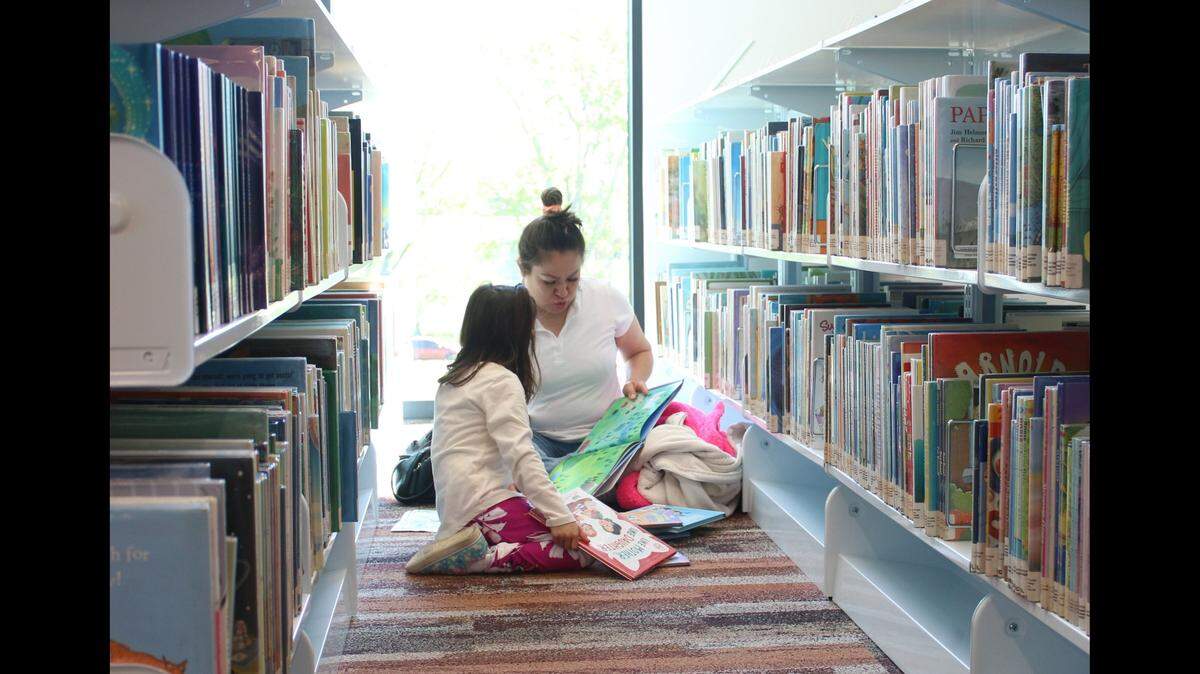 Olathe resident Naomi Olea reads a story to her daughter, 6-year-old Ariana Vela, in the children’s section of the new library in downtown Olathe. The library opened April 29.