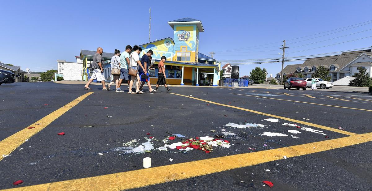 A family walks past the remains of a memorial of flowers, candles, balloons and messages outside the Ride the Ducks offices in Branson. Another memorial soon grew in its place on Saturday.