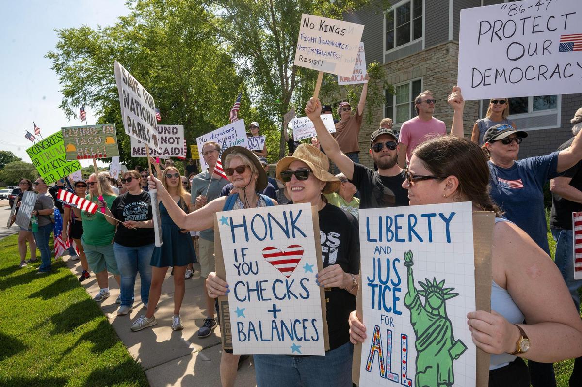 Protesters holding signs lined West 87th Street as part of a nationwide “No Kings” day of defiance on Saturday, June 14, 2025, in Lenexa, Kansas. The events protest President Donald Trump and immigration policies, among other issues.
