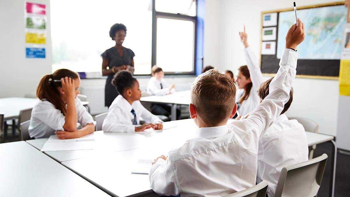 High School Students Wearing Uniform Raising Hands To Answer Question Set By Teacher In Classroom