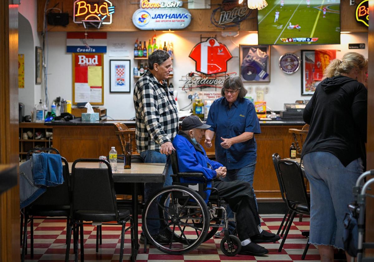 Mike Gergick, left, and Louise Sachen talk with Charles “Jake” Sutulovich, 95, the oldest living member of St. John Catholic Club, during a recent visit. Sutulovich is featured on a poster touting the club’s 100th anniversary. 