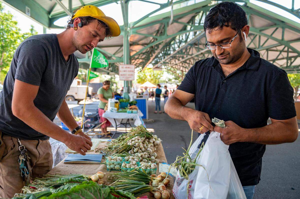 Rakesh Male buys produce from Jameson Hubbard at the Overland Park Farmer’s Market in Overland Park, KS on July 13, 2022.