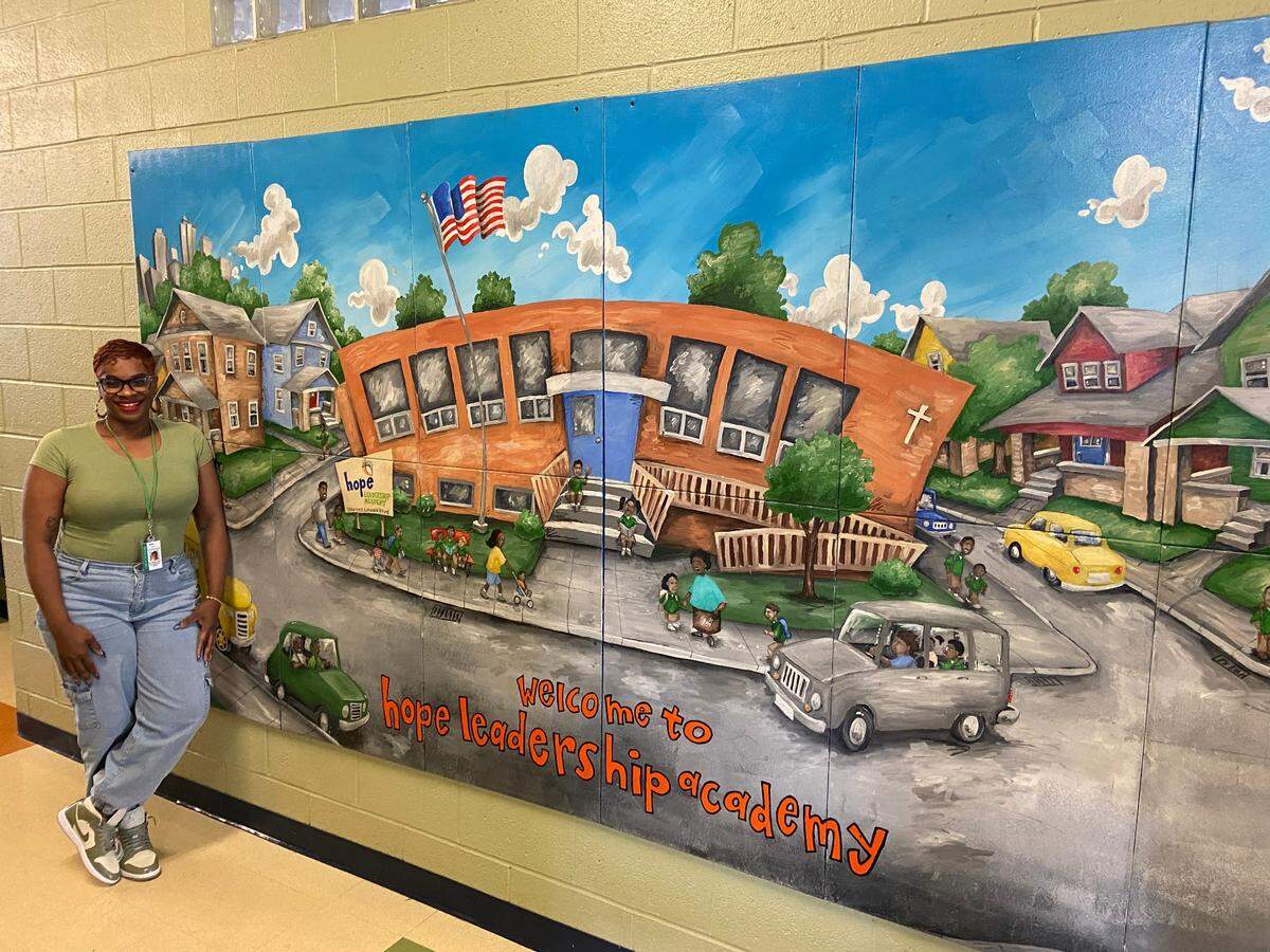 Executive Director Tiffaney Whitt in the hallway of Hope Leadership Academy, in front of a mural portraying the school and the neighborhood.
