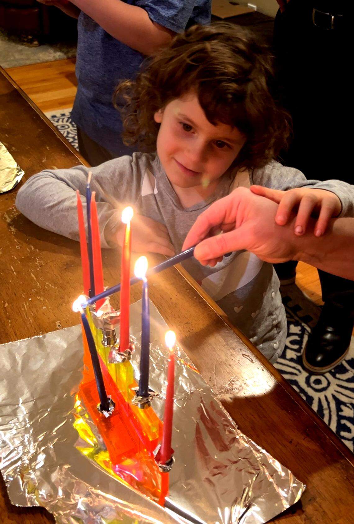 Noah’s little sister, Ella Unell, watches as the candles are lit on a menorah she made with her mom.