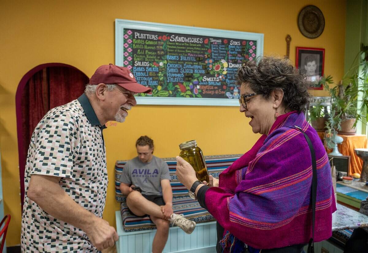 Yahia Kamal, left, also known as “Baba” delights Mercedes Bern-Klug with a large jar of Palestinian olive oil at Baba's Pantry in Kansas City on Tuesday, May 19, 2026. Bern-Klug, visiting from Iowa City, Iowa, extended her trip by a day just to wait for the pantry to open so she could purchase the oil.