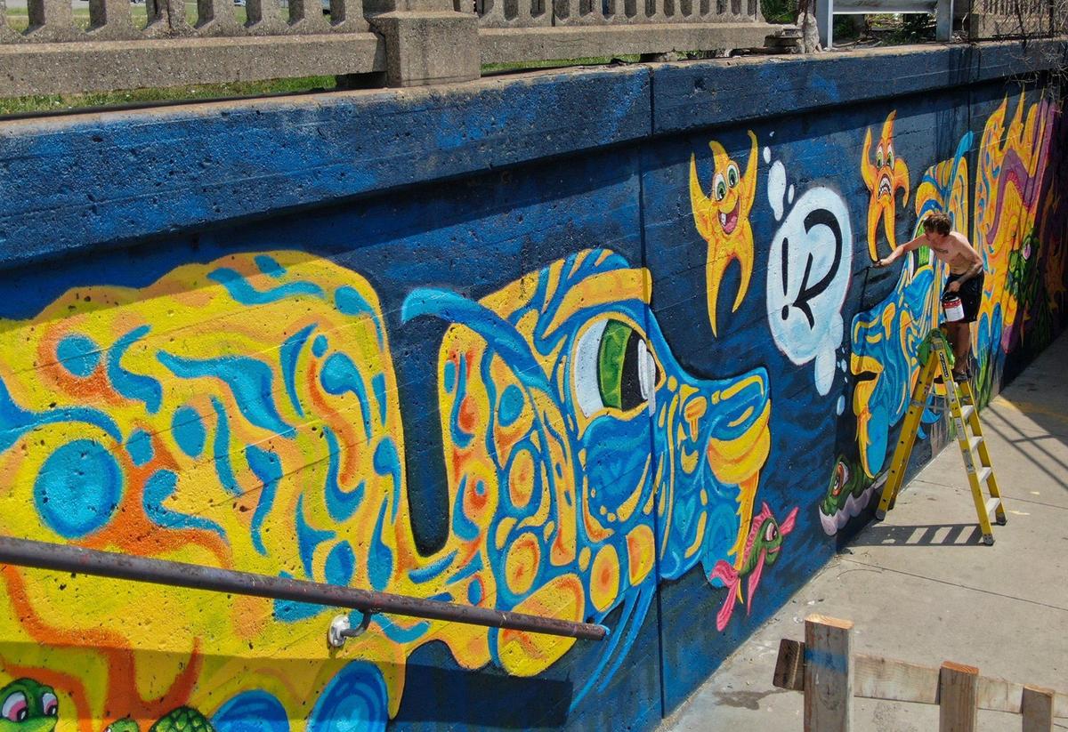 Artist Brian Mapes of We Be More paints a mural he designed on the northwest corner of the Independence Avenue trucking-eating bridge. Mapes, who spent weeks painting the mural, traveled from Lee’s Summit on his scooter to do the painting.
